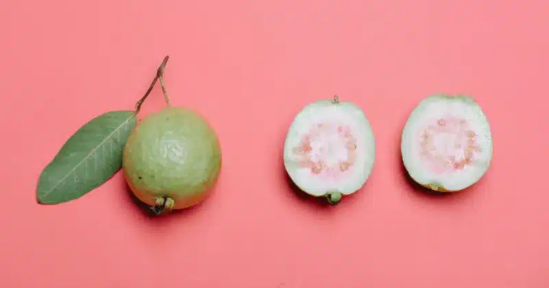 una guayaba entera y una guayaba partida por la mitad sobre un fondo rosa, la guayaba es una deliciosa fruta con g